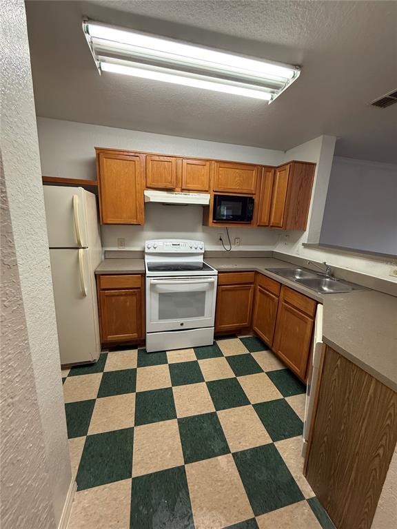 A kitchen features wood cabinets, white appliances, and a green and beige checkered floor — 3712 CASTLE PINES LANE UNIT 4137, ORLANDO, FL