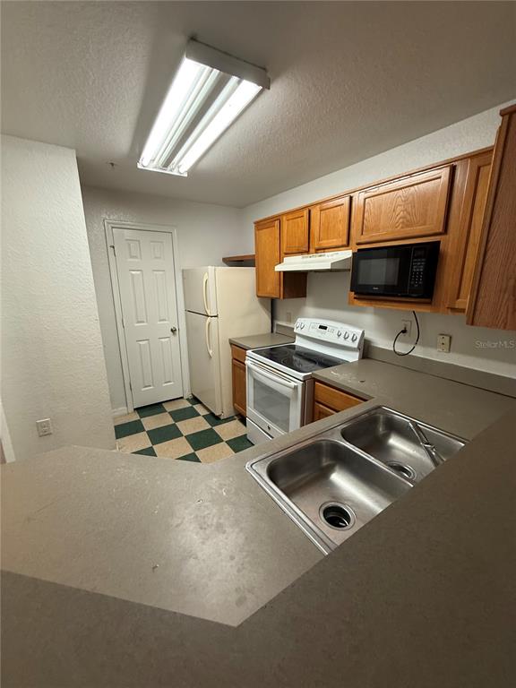 A kitchen features wood cabinets, a white stove, a refrigerator, and a double-basin sink — 3712 CASTLE PINES LANE UNIT 4137, ORLANDO, FL
