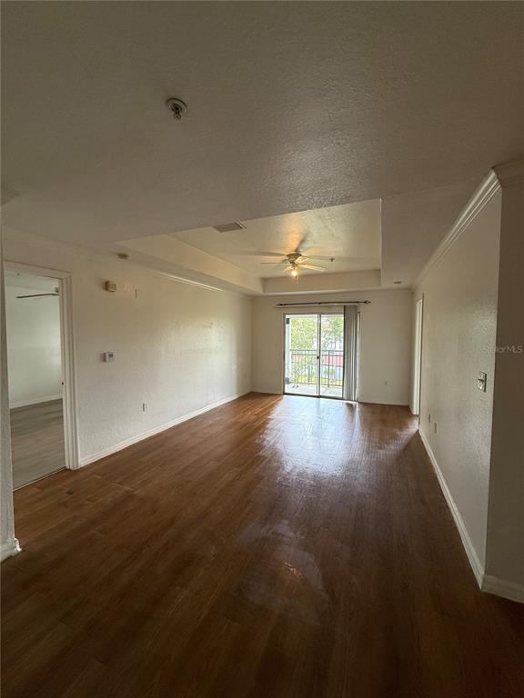 An empty living room features wood-look flooring, a tray ceiling with a fan, and sliding doors — 3712 CASTLE PINES LANE UNIT 4137, ORLANDO, FL