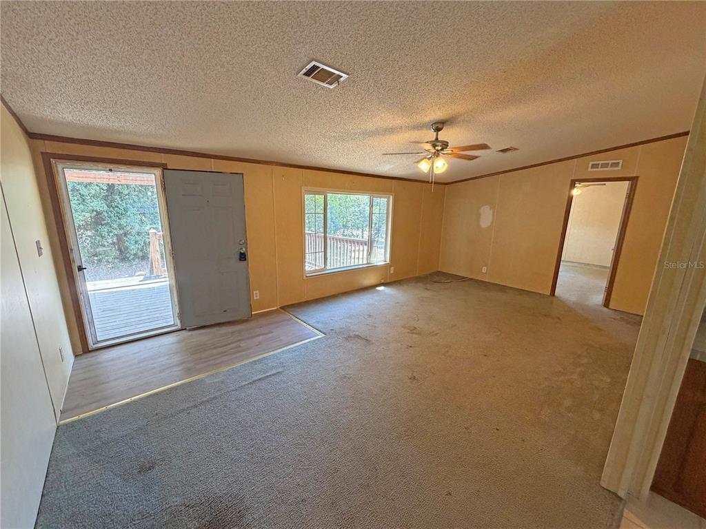 A living room features beige walls, a ceiling fan, carpeted flooring, and a sliding glass door — 120 PEACH, HAWTHORNE, FL