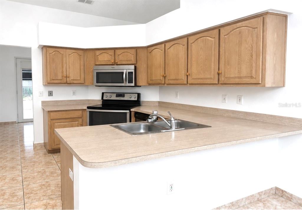 A kitchen features light wood cabinets, laminate countertops, a stainless steel microwave, and tile flooring — 1901 ASHLEY OAKS COURT, ST CLOUD, FL
