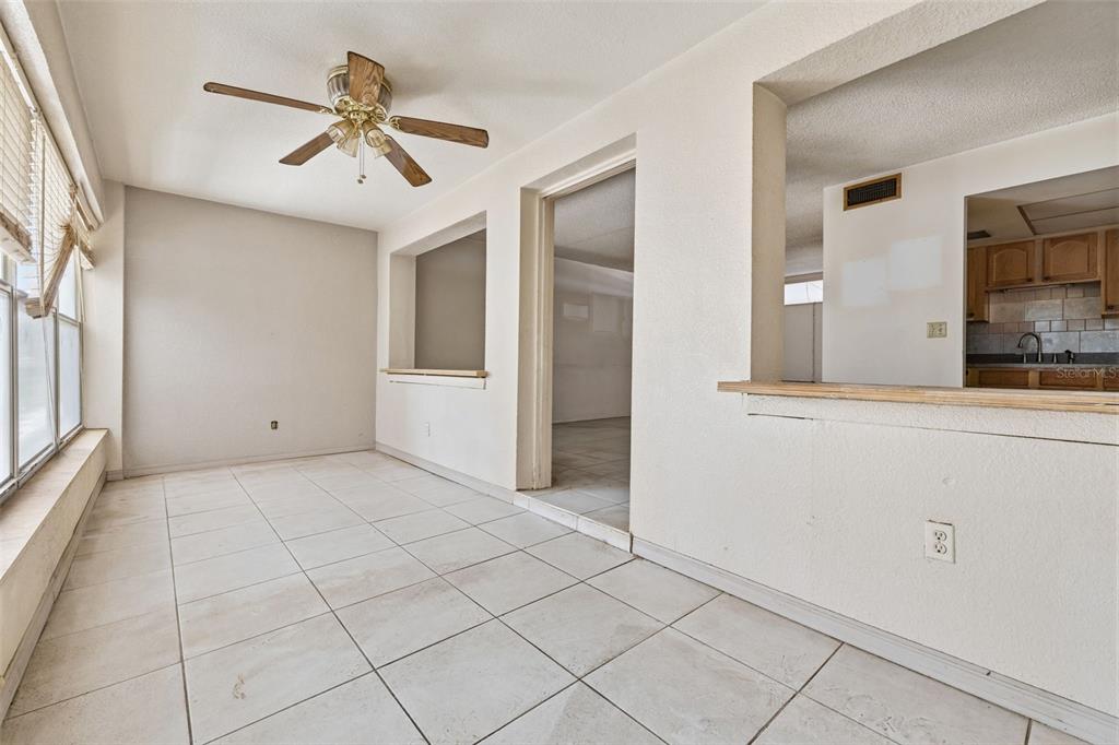 An interior room with white tile flooring, a ceiling fan, and a kitchen pass-through window — 3100 HARTFORD STREET N UNIT 129, ST PETERSBURG, FL