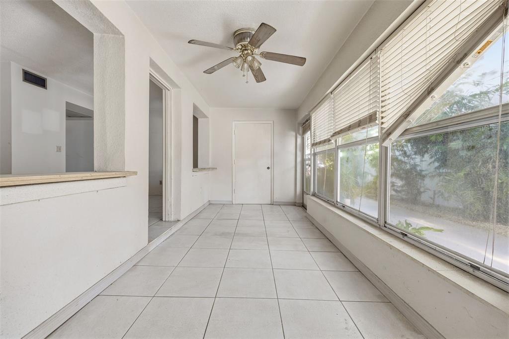 A sunroom with white tile floors, a ceiling fan, and large windows overlooking greenery — 3100 HARTFORD STREET N UNIT 129, ST PETERSBURG, FL