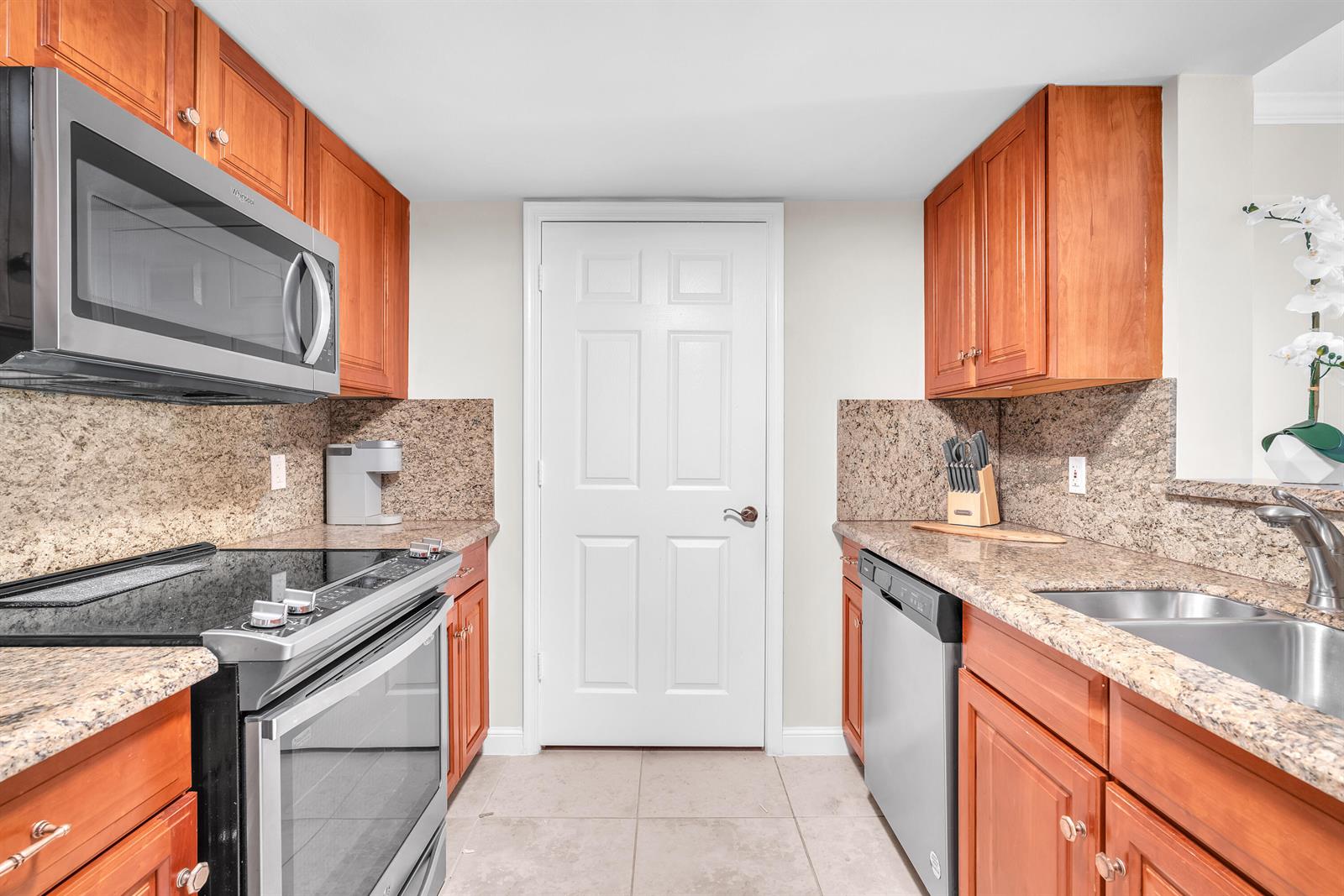 A galley kitchen features wood cabinets, granite countertops, stainless steel appliances, and a white door — 101 Plaza Real, Boca Raton FL 33432, BOCA RATON, FL