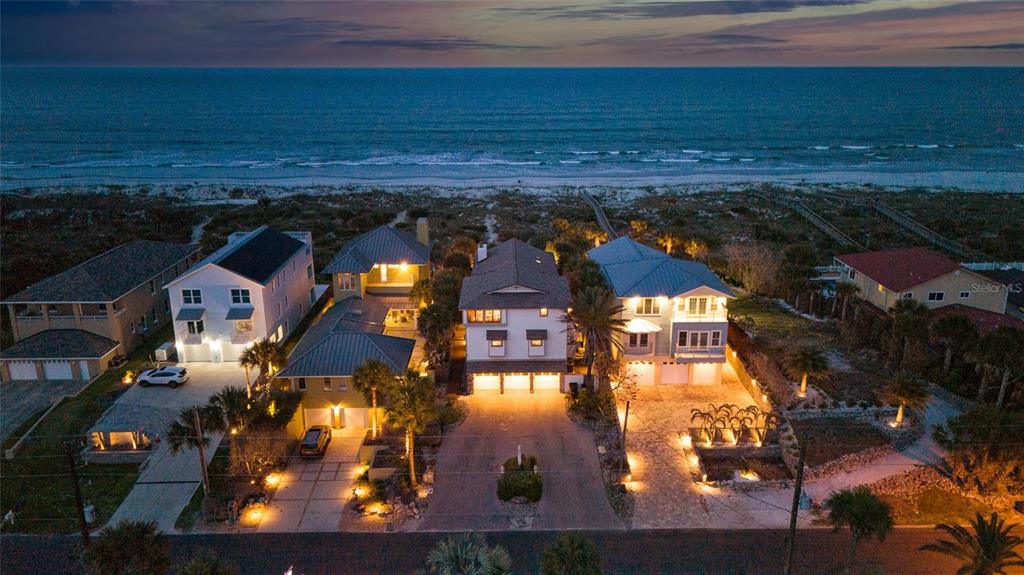 An aerial view shows several multi-story beachfront houses at dusk along a sandy coastline — 1421 N ATLANTIC AVENUE, NEW SMYRNA BEACH, FL