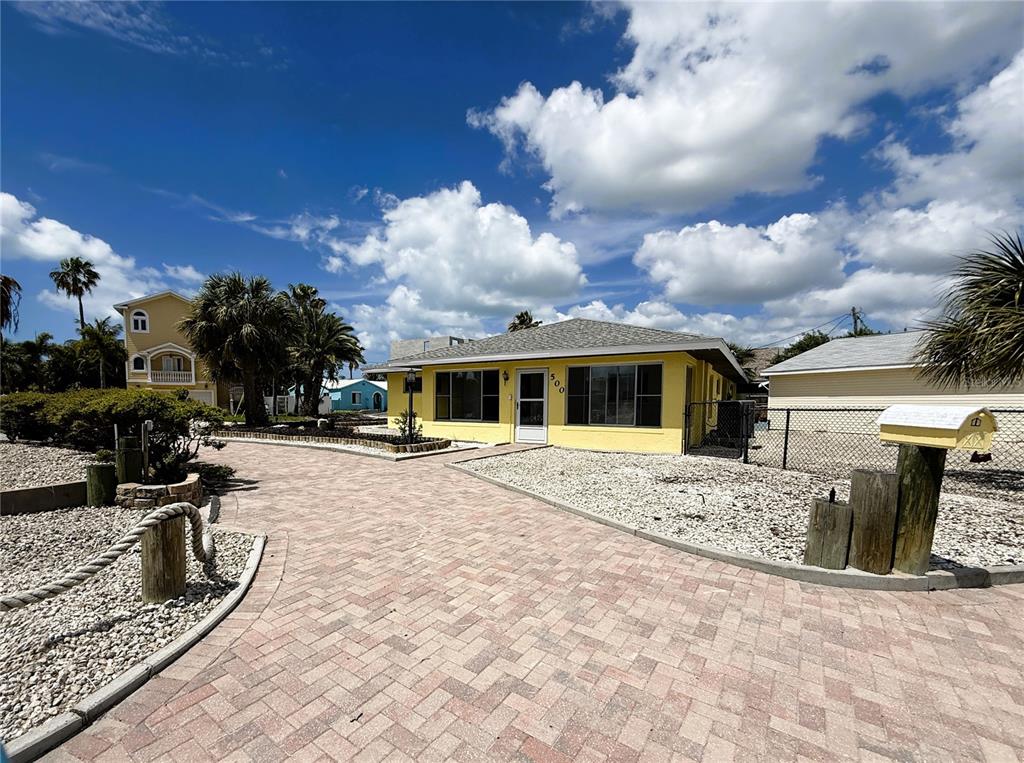 A yellow single-story house features a brick paver driveway and a white mailbox — 500 140TH AVENUE E, MADEIRA BEACH, FL