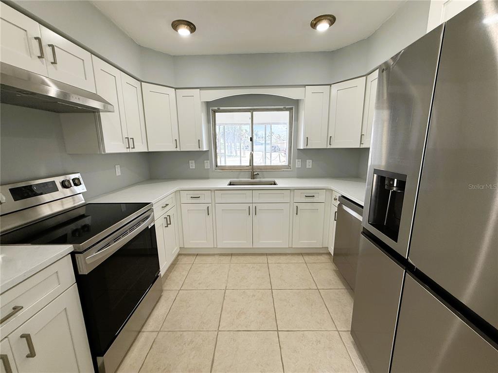A kitchen features white cabinets, stainless steel appliances, light countertops, and beige tile flooring — 500 140TH AVENUE E, MADEIRA BEACH, FL