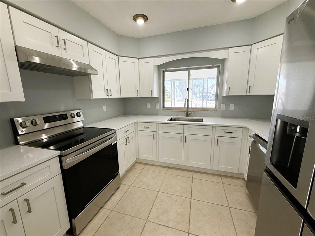 A kitchen features white cabinets, stainless steel appliances, light countertops, and beige tile flooring — 500 140TH AVENUE E, MADEIRA BEACH, FL