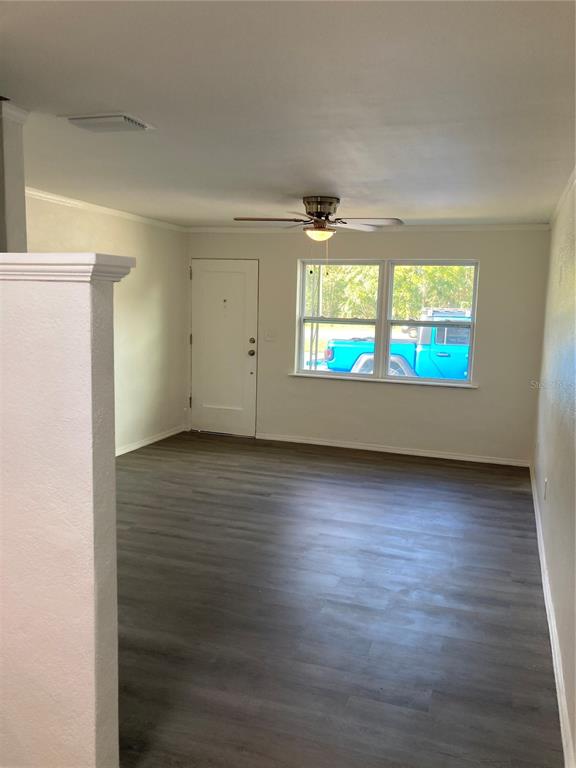 An empty room features gray wood-look flooring, a ceiling fan, and a white entry door — 5221 N RONALD REAGAN BOULEVARD, SANFORD, FL