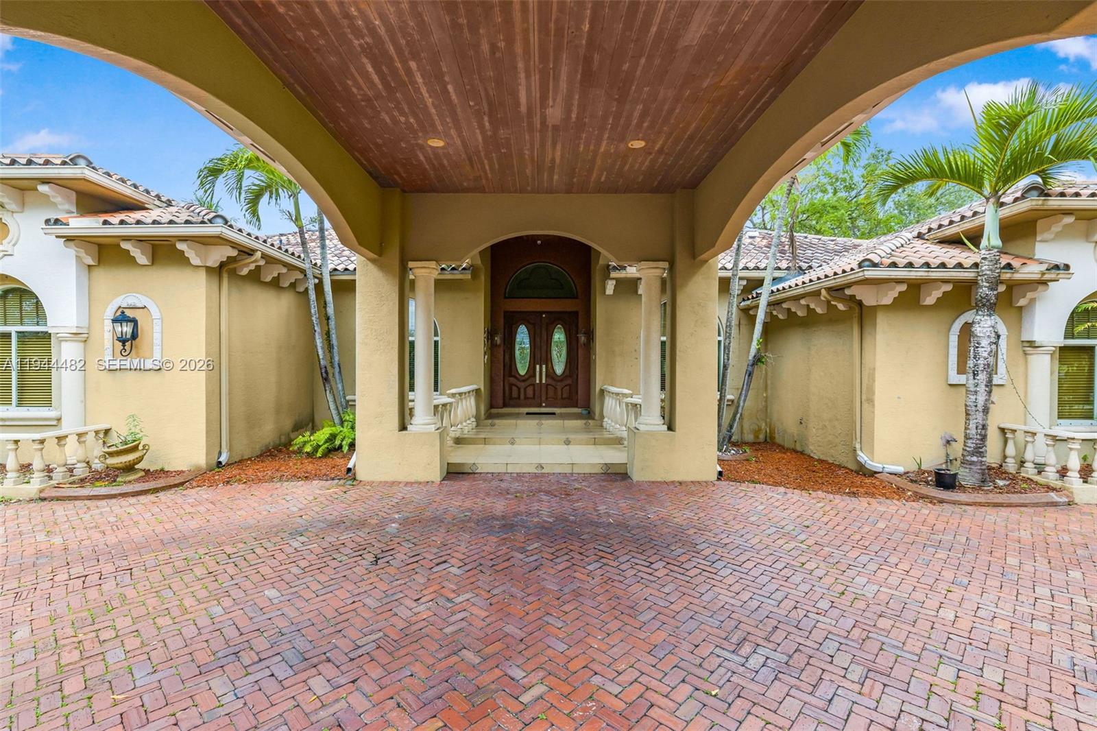 A brick driveway leads to the covered entrance of a tan house with double doors — 7761 SW 122nd Ave, Miami FL 33183, MIAMI, FL