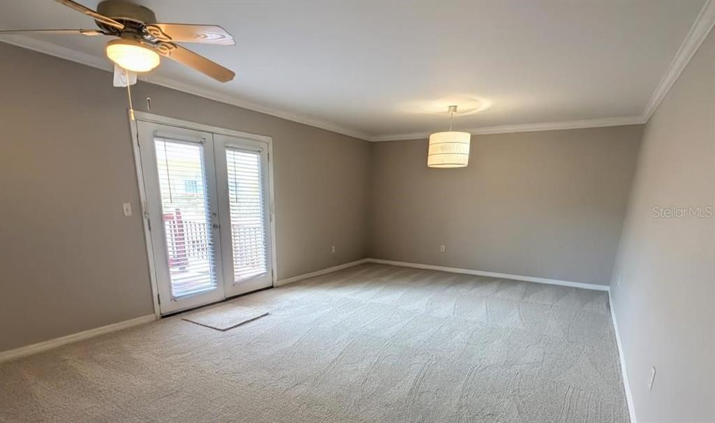 An empty room with beige carpet, a ceiling fan, a pendant light, and glass doors — 1841 PARAKEET WAY UNIT 1101, SARASOTA, FL