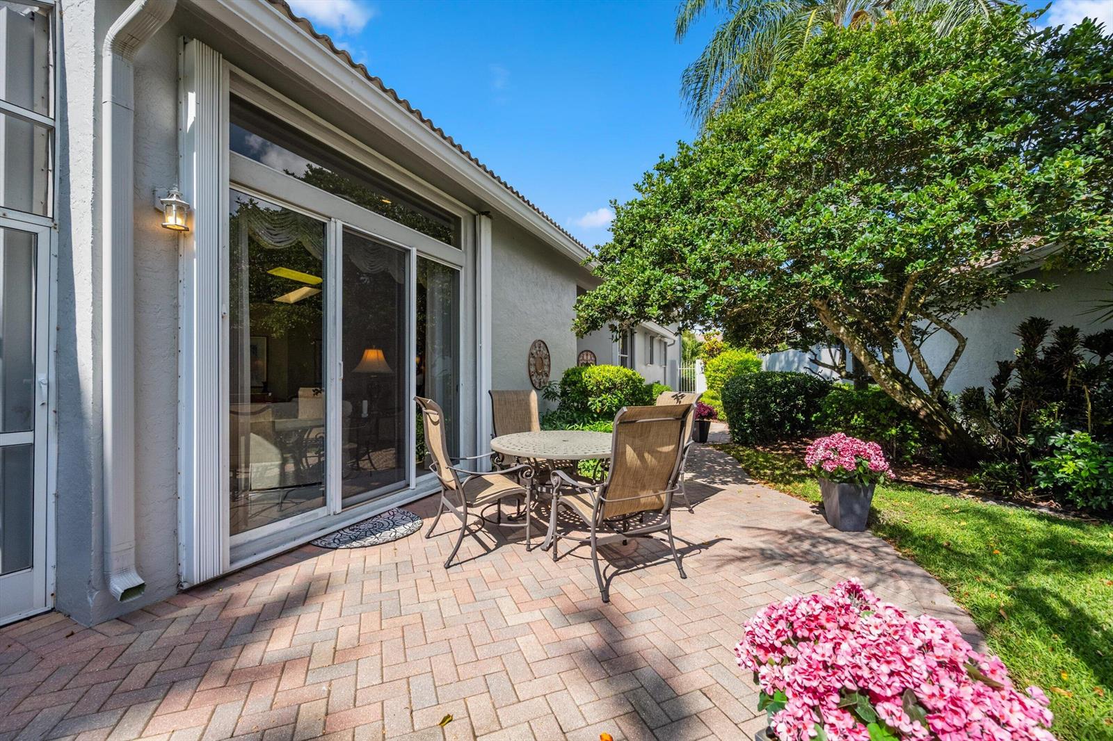A paved patio features a dining set outside a house with sliding glass doors — 4730 Carlton Golf Drive, Lake Worth FL 33449, LAKE WORTH, FL