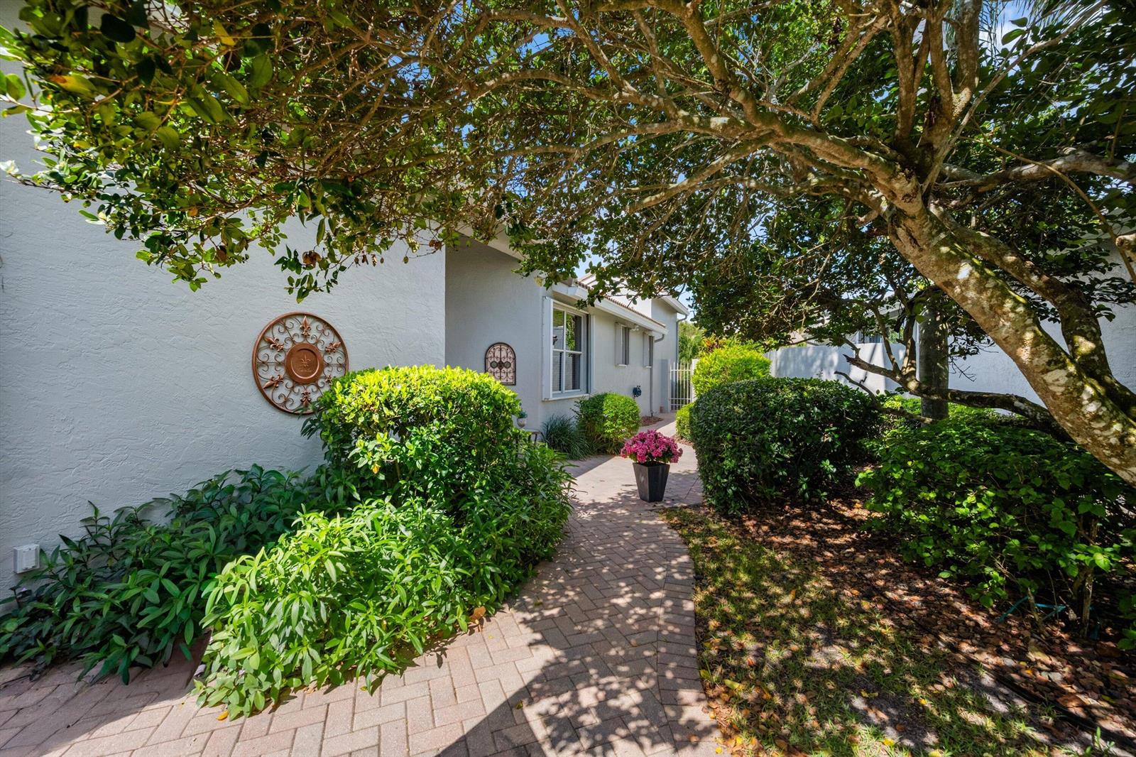 A paved walkway leads to a house entrance surrounded by lush green bushes and trees — 4730 Carlton Golf Drive, Lake Worth FL 33449, LAKE WORTH, FL