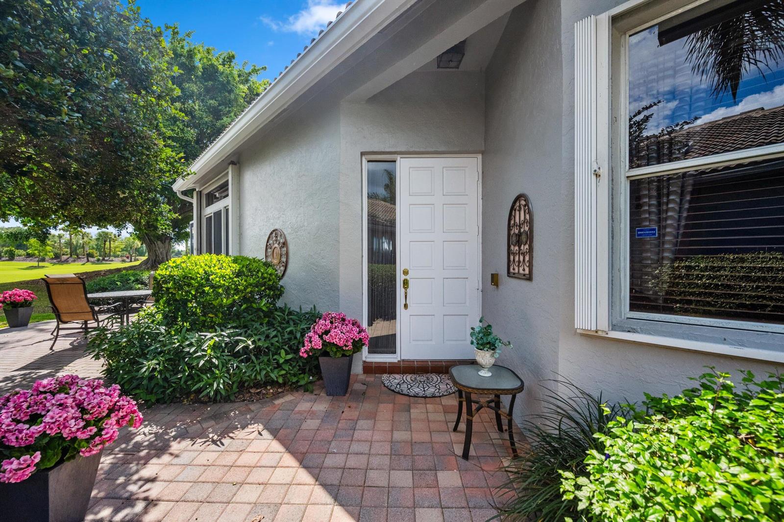 A white front door with a sidelight opens onto a brick patio with potted flowers — 4730 Carlton Golf Drive, Lake Worth FL 33449, LAKE WORTH, FL