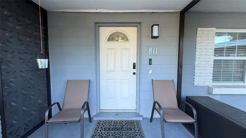 A gray front porch features a white door, two chairs, and a patterned wall panel — 811 22ND STREET NW, WINTER HAVEN, FL