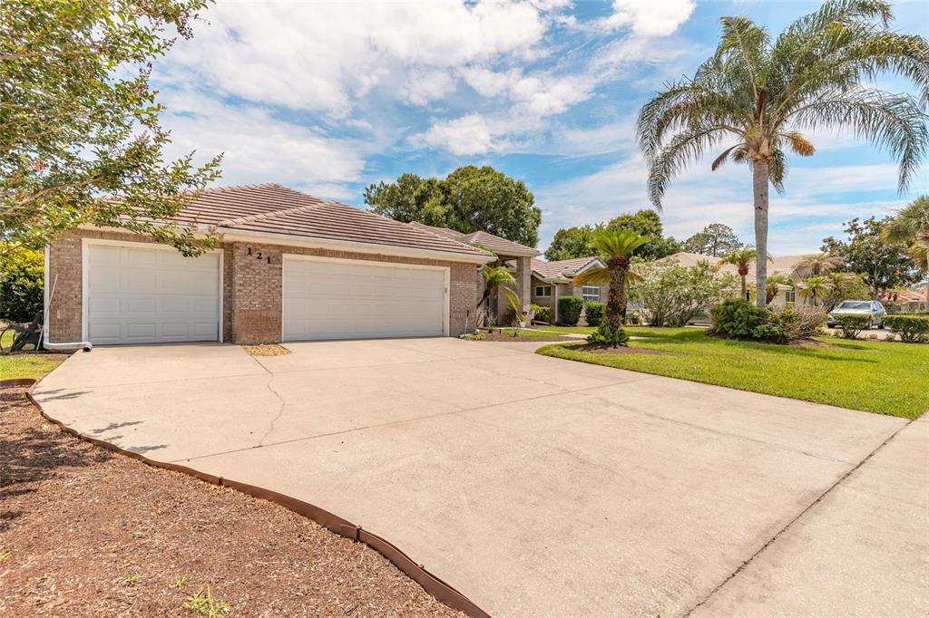 A single-story brick house with a three-car garage and a large concrete driveway — 121 KING EIDER COURT, DAYTONA BEACH, FL