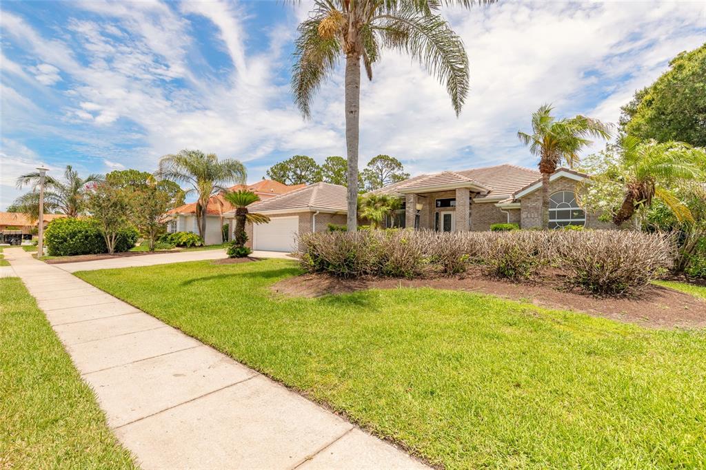 A single-story brick house with a tiled roof, palm trees, and a concrete sidewalk — 121 KING EIDER COURT, DAYTONA BEACH, FL