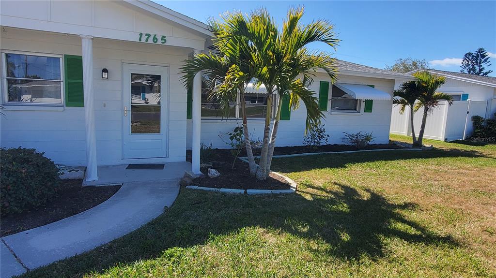 A white house exterior features green shutters, a palm tree, and a covered front porch — 1765 LORALIN DRIVE, ENGLEWOOD, FL