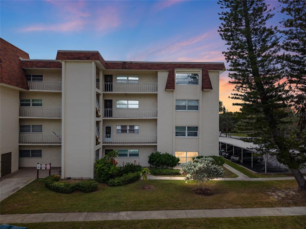 A multi-story apartment building with balconies and a covered parking area at sunset — 209 NE LINCOLN CIRCLE N UNIT 109, ST PETERSBURG, FL
