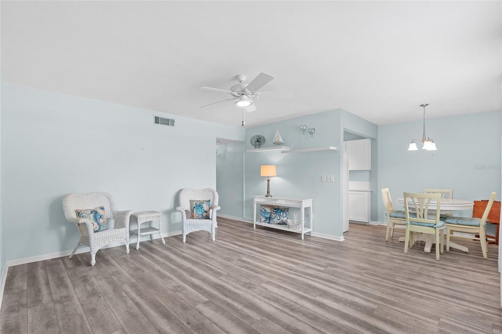 A living and dining area features light blue walls, wood-look flooring, and white wicker furniture — 209 NE LINCOLN CIRCLE N UNIT 109, ST PETERSBURG, FL