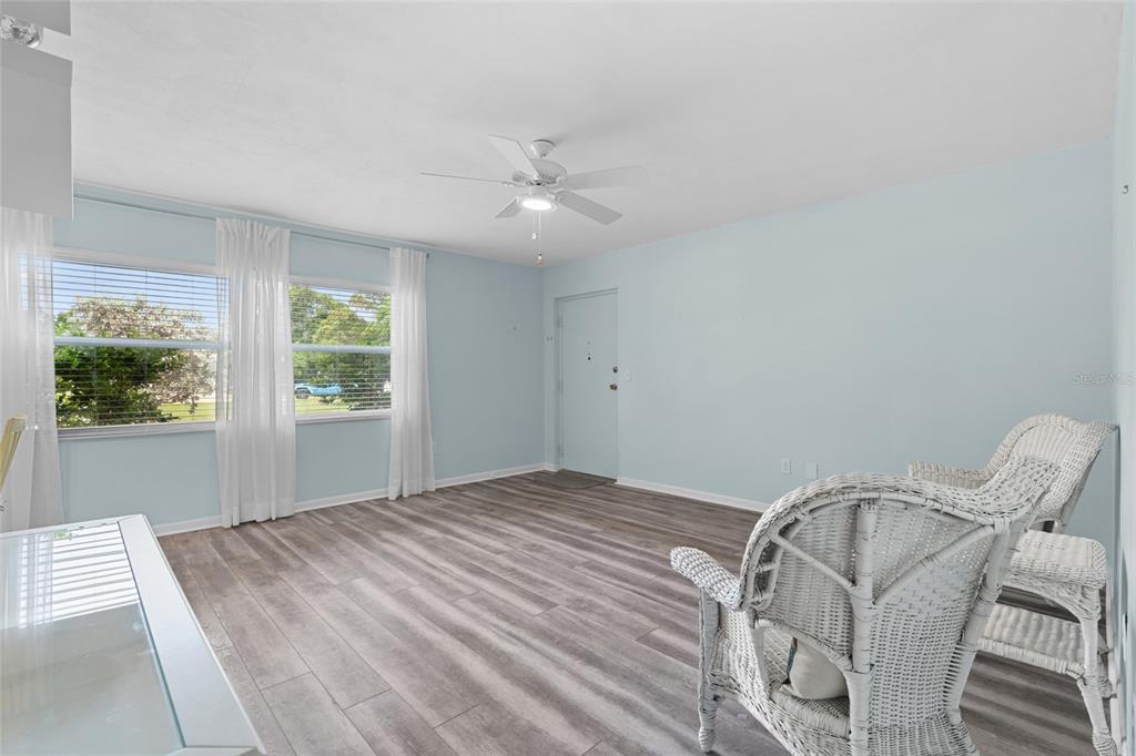 A living room with light blue walls, wood-look flooring, a ceiling fan, and wicker chairs — 209 NE LINCOLN CIRCLE N UNIT 109, ST PETERSBURG, FL