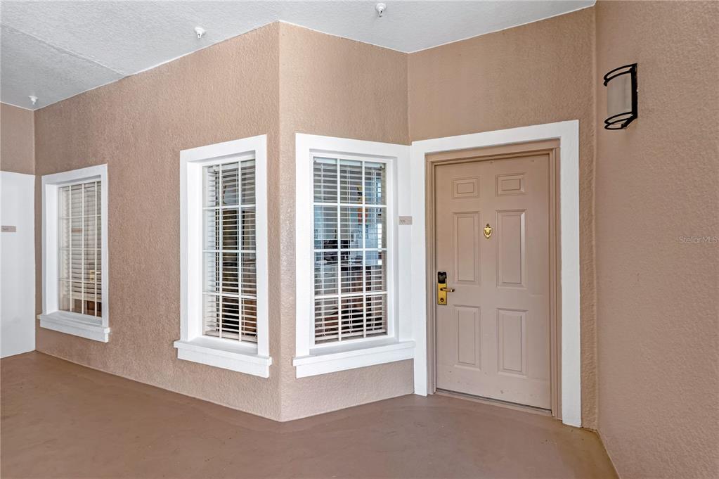 A tan exterior entryway features a front door, two windows with white shutters, and stucco walls — 8601 WORLDQUEST BOULEVARD UNIT 3506, ORLANDO, FL