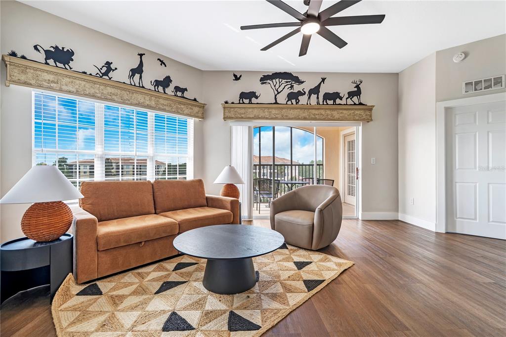 A living room features a brown sofa, a round coffee table, and safari-themed wall decals — 8601 WORLDQUEST BOULEVARD UNIT 3506, ORLANDO, FL