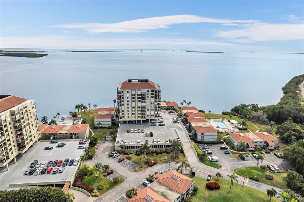 An aerial view shows a multi-story residential complex with parking lots situated along a bay — 6372 PALMA DEL MAR BOULEVARD S UNIT 406, ST PETERSBURG, FL