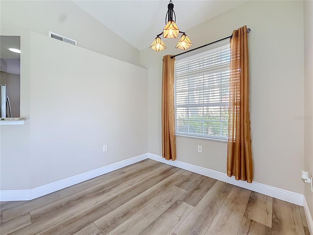 An empty dining area features light wood-look flooring, a window with gold curtains, and lighting — 5281 BOWLINE COURT, OXFORD, FL