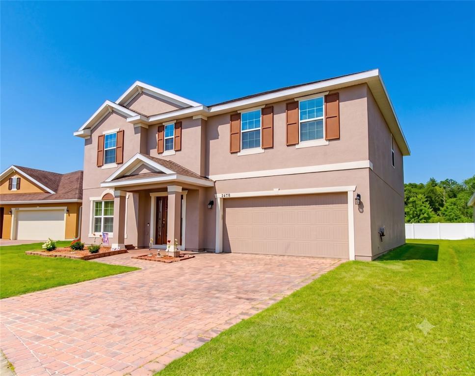 A two-story suburban house with a tan stucco exterior, brown shutters, and a paved driveway — 2478 ADDISON CREEK DRIVE, KISSIMMEE, FL
