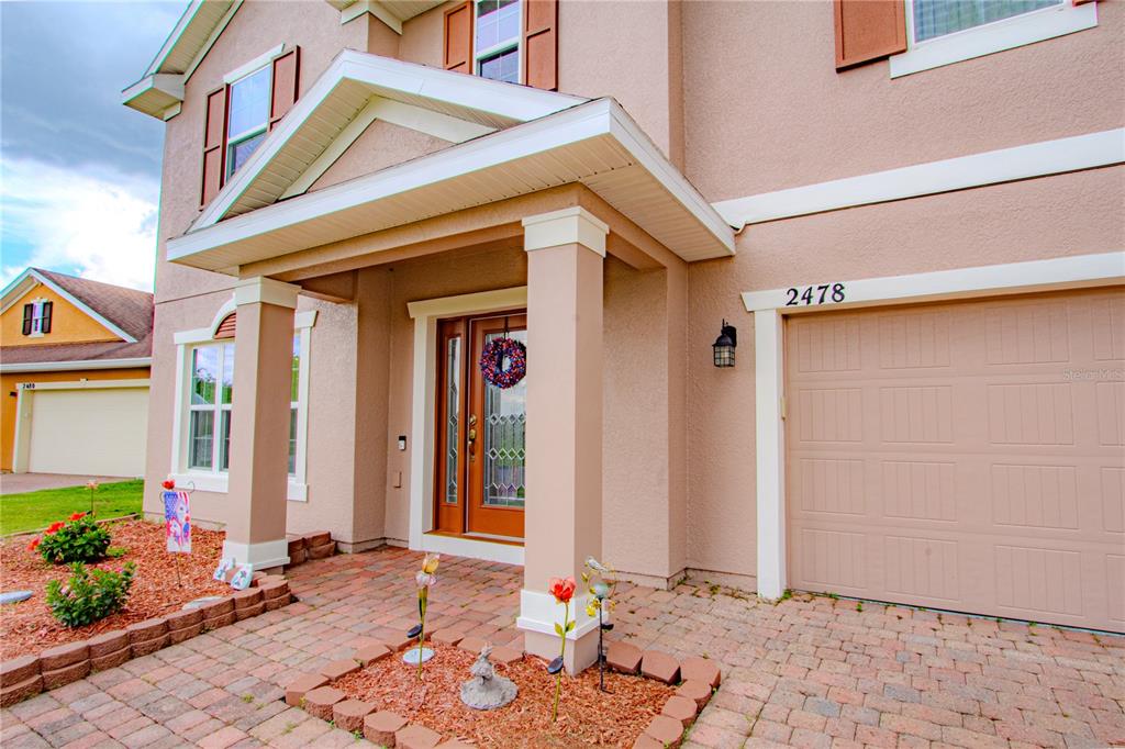 A tan two-story house features a brick paver walkway, a covered porch, and a garage — 2478 ADDISON CREEK DRIVE, KISSIMMEE, FL