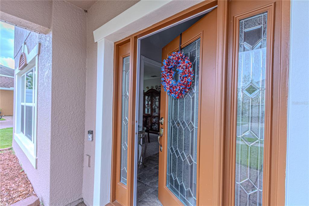 A partially open front door with a decorative wreath leads into a home interior — 2478 ADDISON CREEK DRIVE, KISSIMMEE, FL