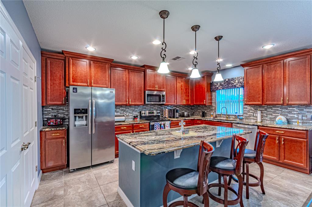 A kitchen features wood cabinets, stainless steel appliances, a granite island, and tile flooring — 2478 ADDISON CREEK DRIVE, KISSIMMEE, FL