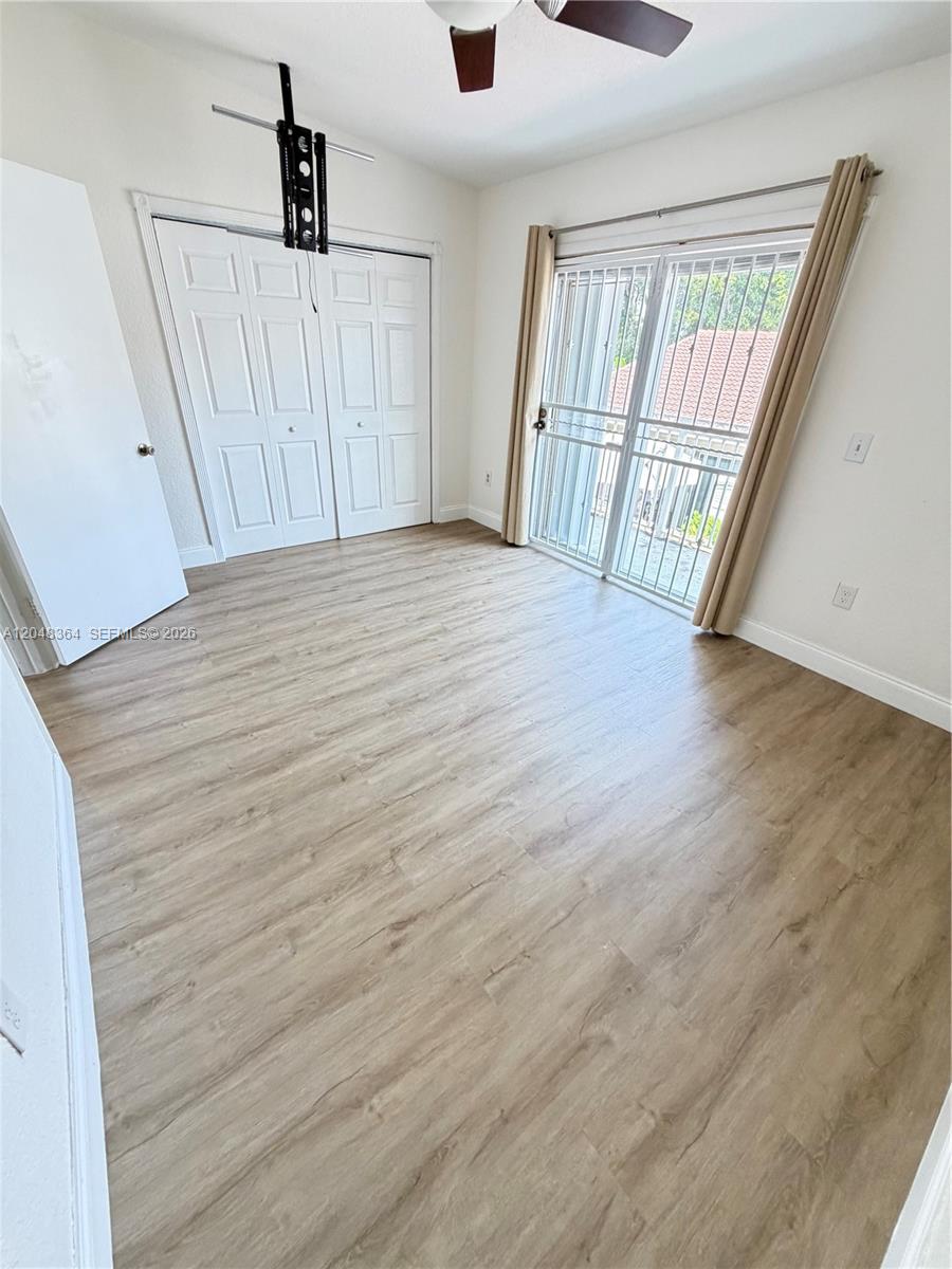 This bedroom features light wood-look flooring, white closet doors, and a sliding glass door — 6926 NW 166th Ter # 1302, Miami Lakes FL 33014, MIAMI LAKES, FL