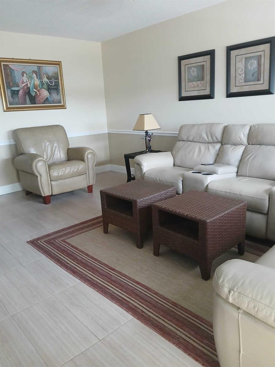 A living room features light-colored tile floors, a leather sofa and armchair, and wicker tables — 4023 Newport H, Deerfield Beach FL 33442, DEERFIELD BEACH, FL