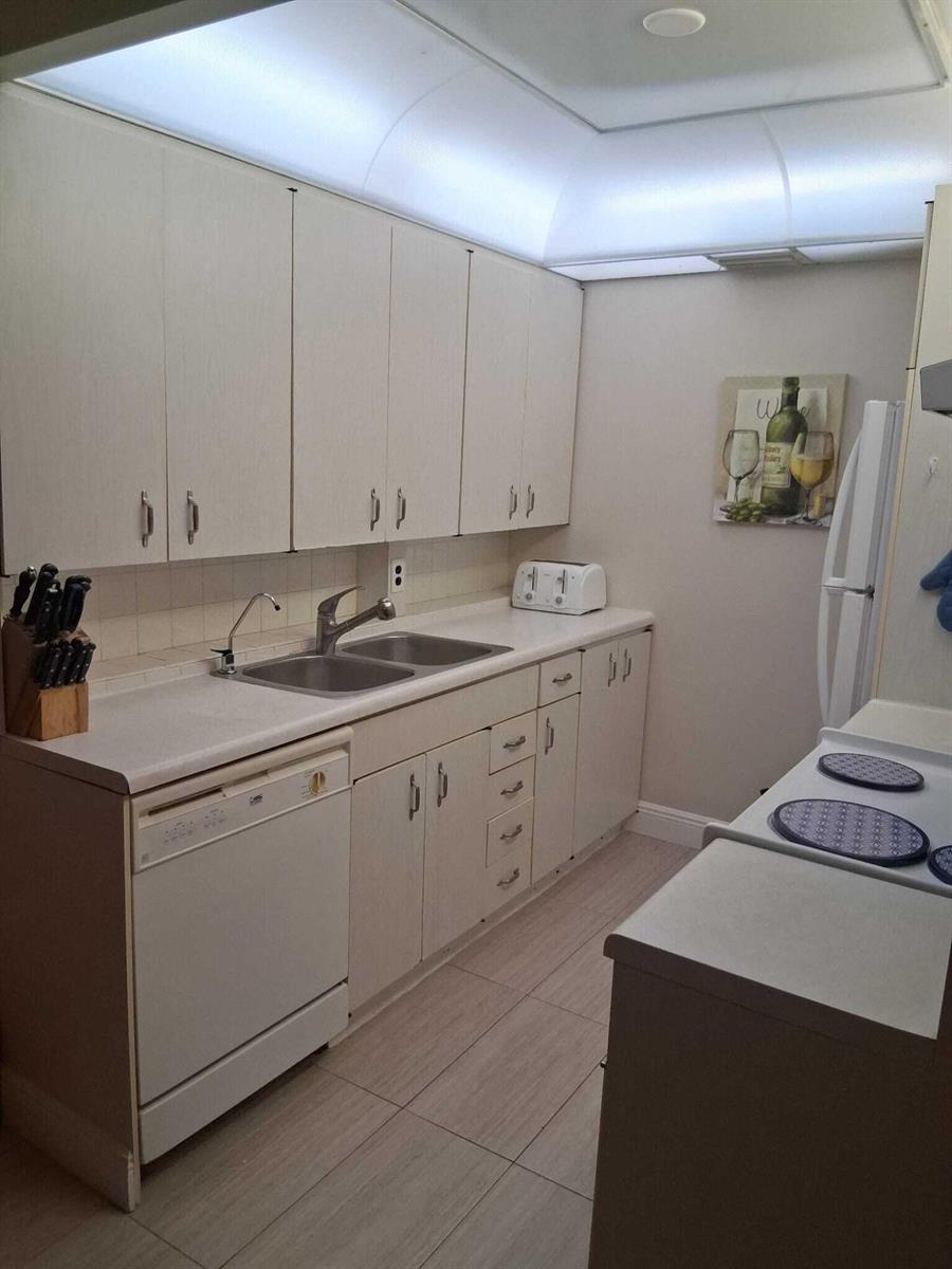 A galley kitchen features white cabinets, a double sink, a dishwasher, and light-colored tile flooring — 4023 Newport H, Deerfield Beach FL 33442, DEERFIELD BEACH, FL