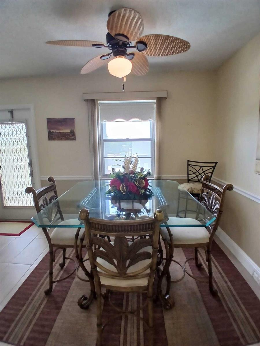 A dining room features a glass-topped table, wicker-style chairs, a ceiling fan, and a window — 4023 Newport H, Deerfield Beach FL 33442, DEERFIELD BEACH, FL