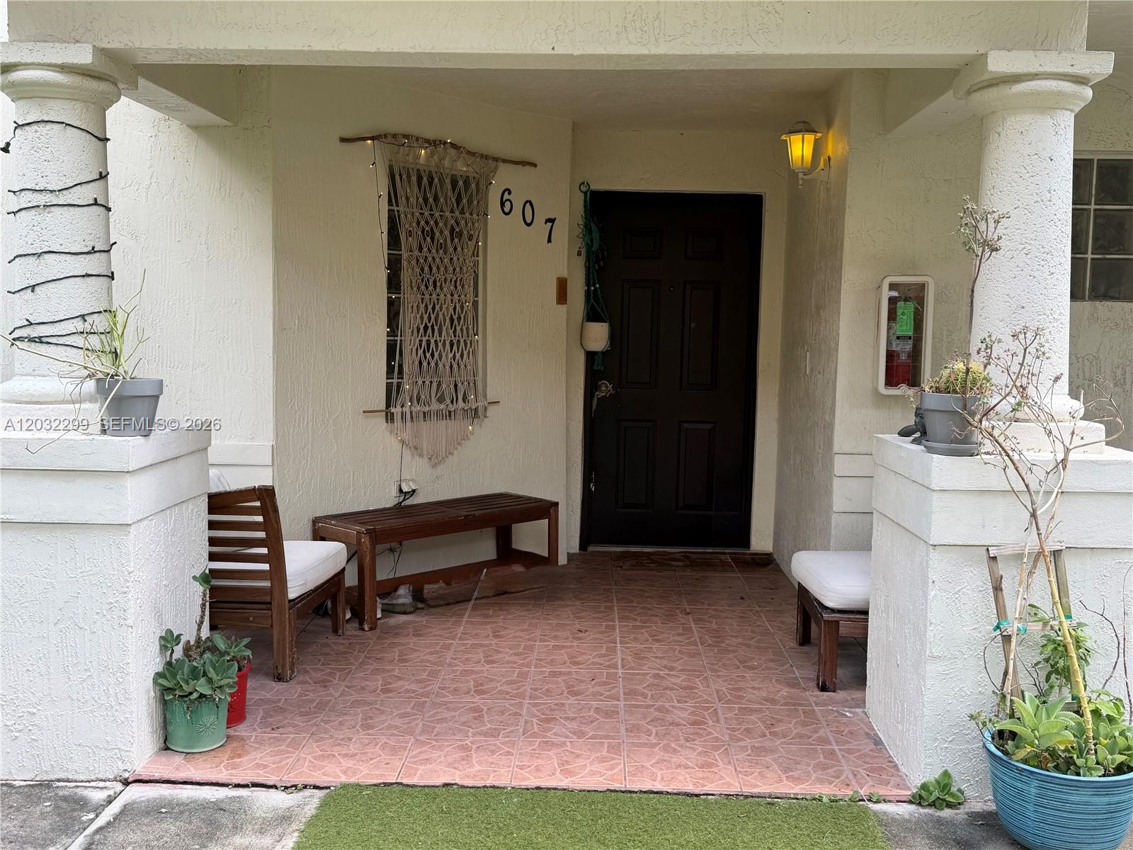 A covered front porch features a dark door, tiled flooring, wooden benches, and potted plants — 8802 NW 109th Ct # 607, Doral FL 33178, DORAL, FL