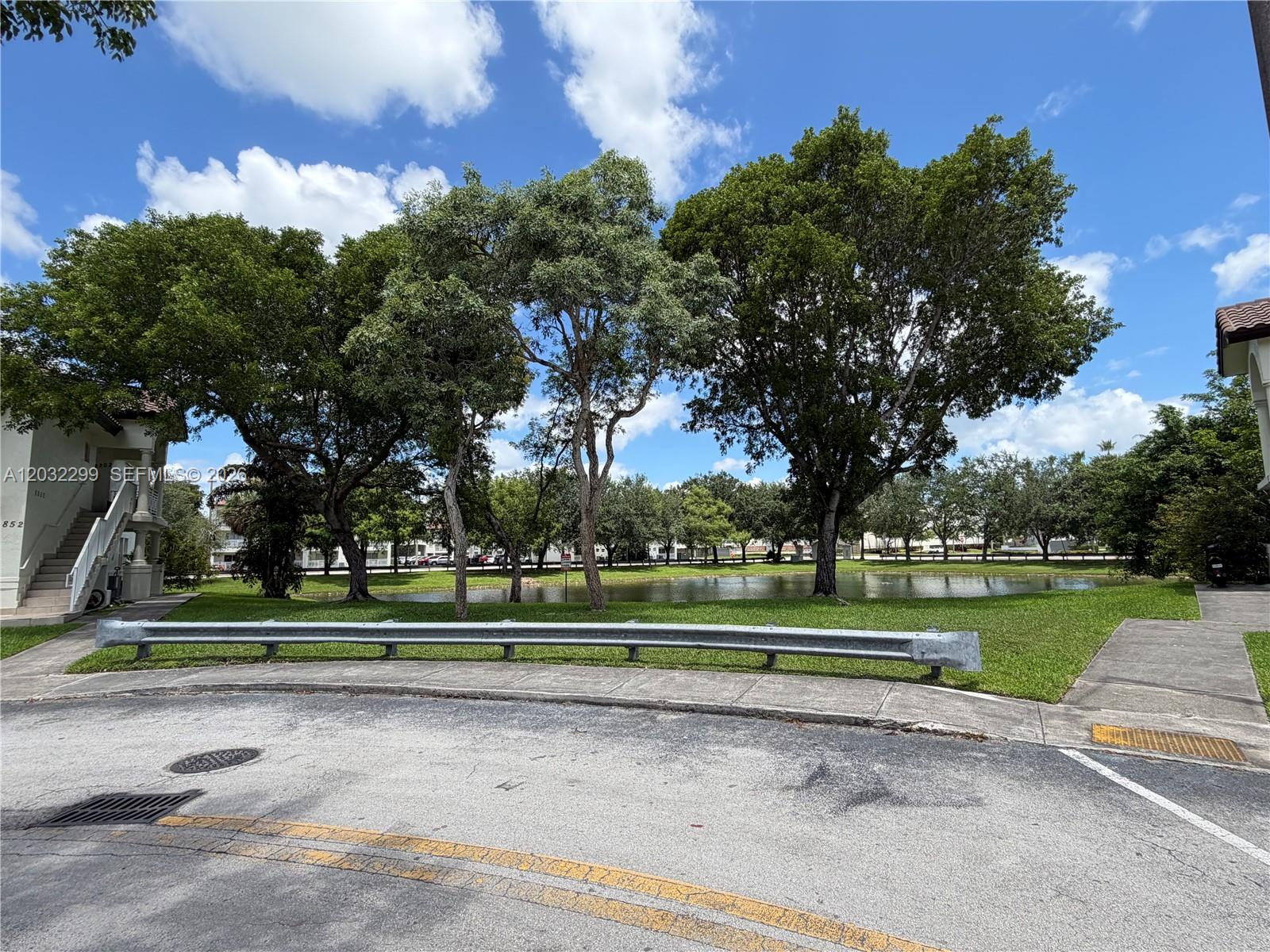 A metal guardrail sits in front of a grassy lawn, a pond, and large trees — 8802 NW 109th Ct # 607, Doral FL 33178, DORAL, FL