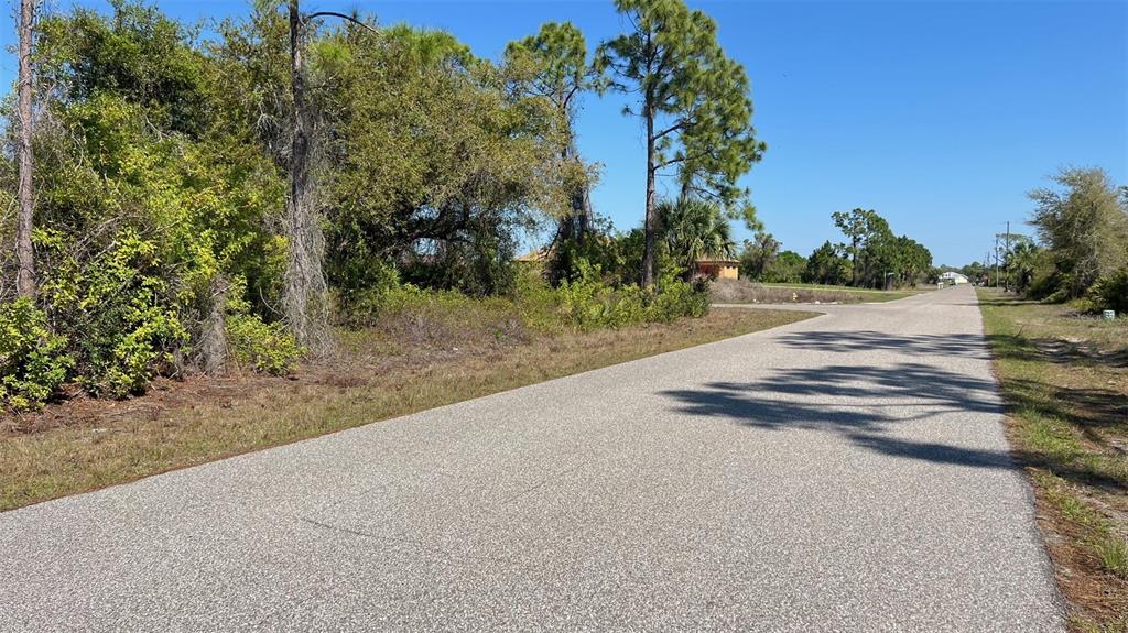 An asphalt road runs alongside a vacant, wooded lot under a clear blue sky — 4397 KENNEL STREET, PORT CHARLOTTE, FL