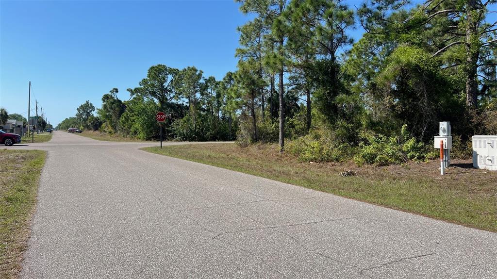 A paved road leads to a stop sign at an intersection near a wooded lot — 4397 KENNEL STREET, PORT CHARLOTTE, FL