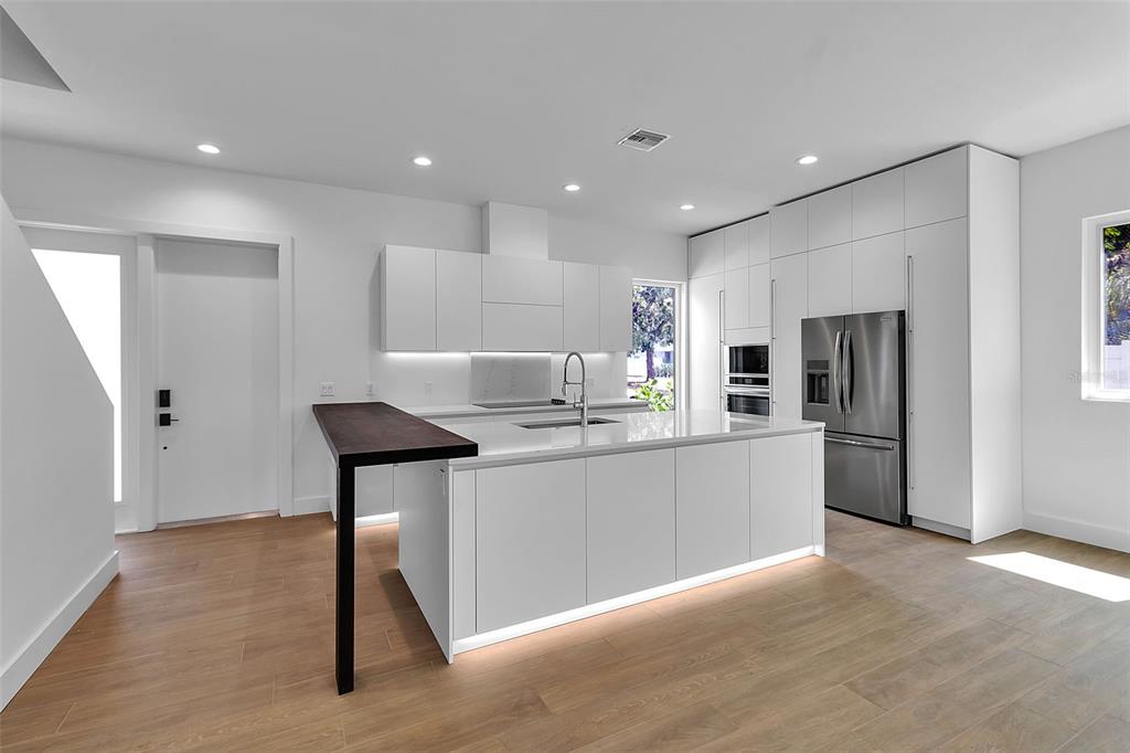 A modern kitchen features white flat-panel cabinetry, a central island with a dark wood breakfast bar — 2516 BROWNING STREET, SARASOTA, FL