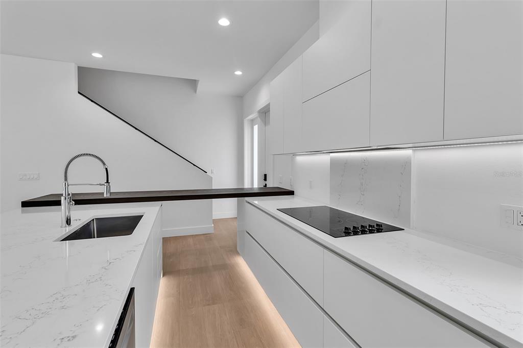 A modern kitchen features white cabinetry, marble countertops, and a dark wood breakfast bar — 2516 BROWNING STREET, SARASOTA, FL
