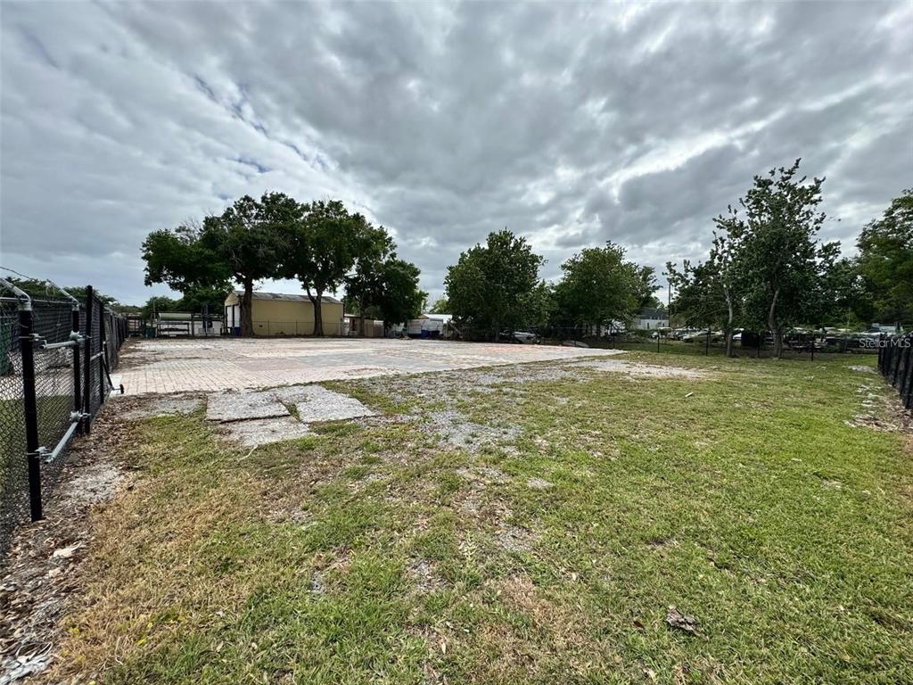 A fenced, vacant lot features a paved area and scattered trees under a cloudy sky — 580 FAIRVILLA ROAD, ORLANDO, FL