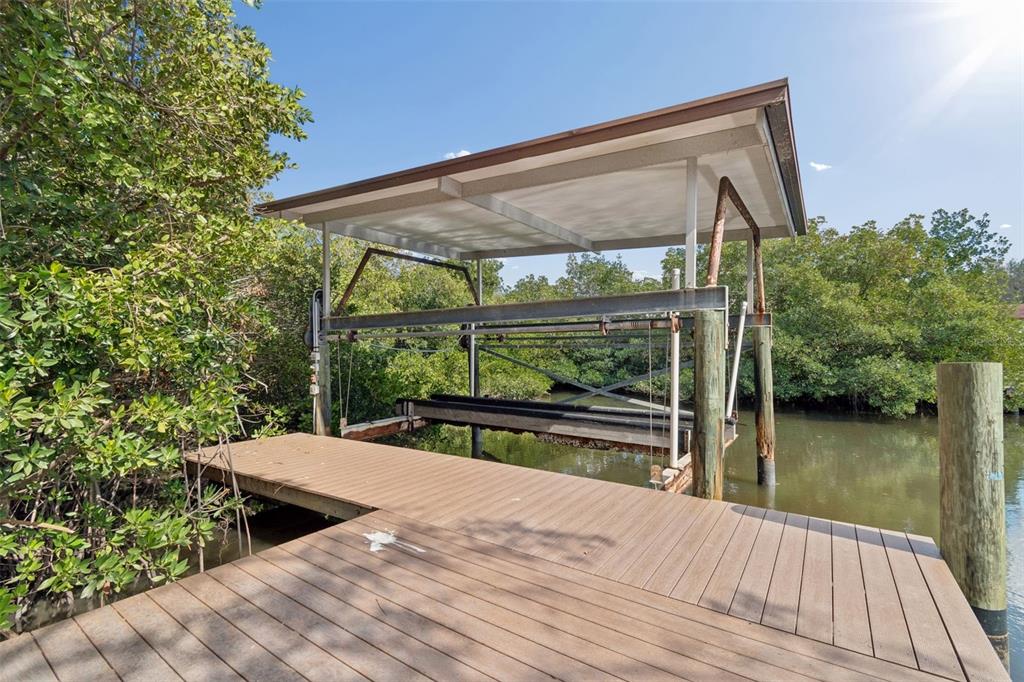 A wooden dock features a covered boat lift structure surrounded by dense green trees — 8402 BOXWOOD DRIVE, TAMPA, FL