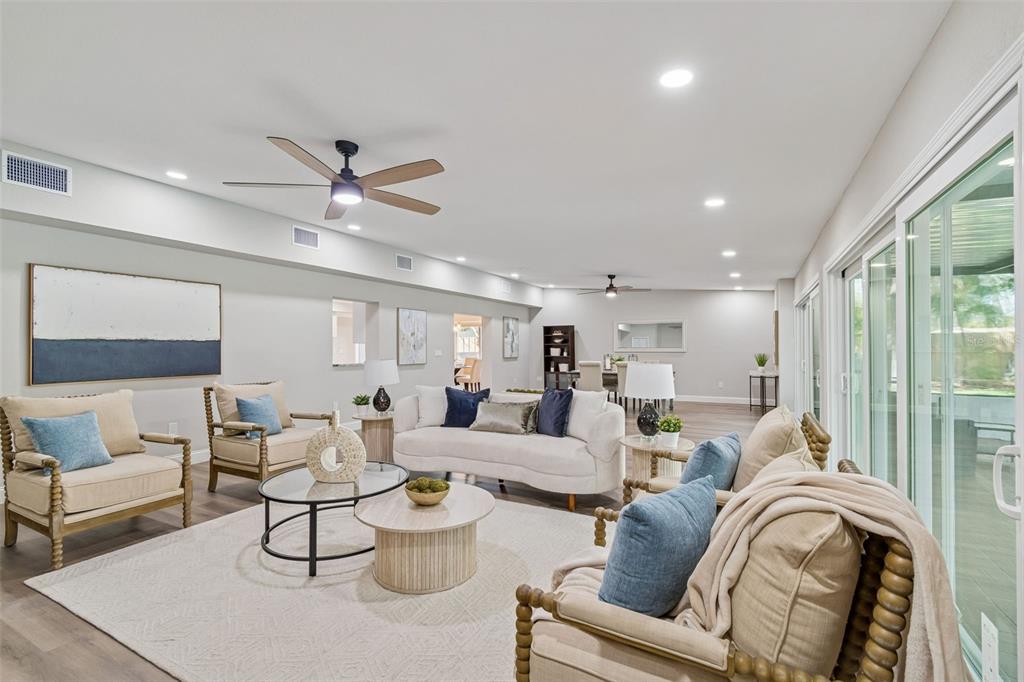 A spacious living room features neutral furniture, a ceiling fan, and sliding glass patio doors — 8402 BOXWOOD DRIVE, TAMPA, FL