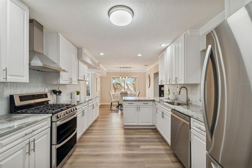 A kitchen with white cabinets, stainless steel appliances, and wood-look flooring leads to a dining area — 8402 BOXWOOD DRIVE, TAMPA, FL