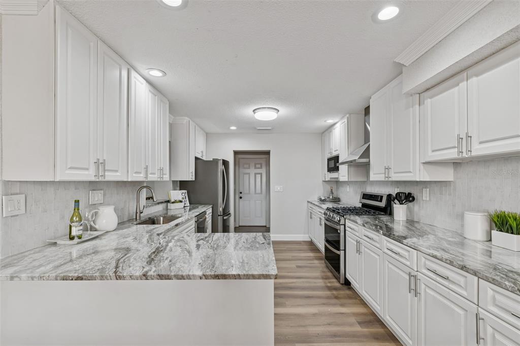 A kitchen features white cabinets, marble-patterned countertops, stainless steel appliances, and wood-look flooring — 8402 BOXWOOD DRIVE, TAMPA, FL
