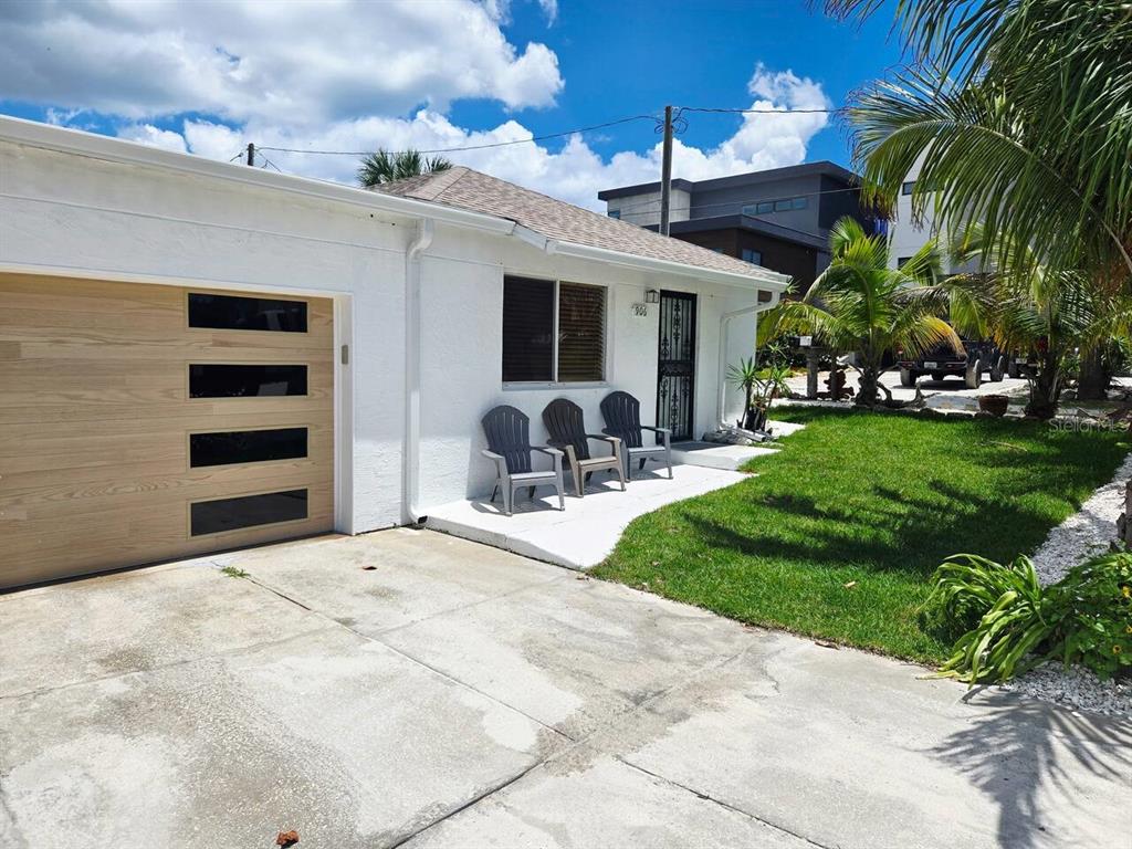 A white house with a wood-paneled garage door and three chairs on the front porch — 906 E 11TH AVENUE, NEW SMYRNA BEACH, FL