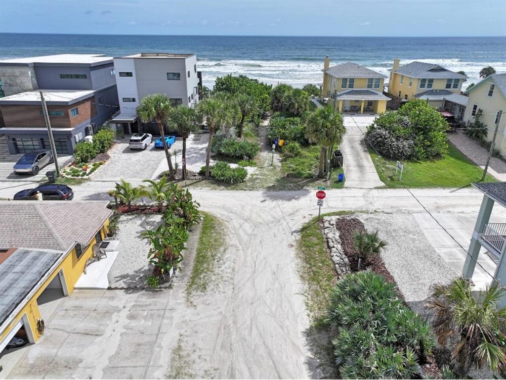 An aerial view shows a sandy road leading toward a beach with several coastal houses — 906 E 11TH AVENUE, NEW SMYRNA BEACH, FL
